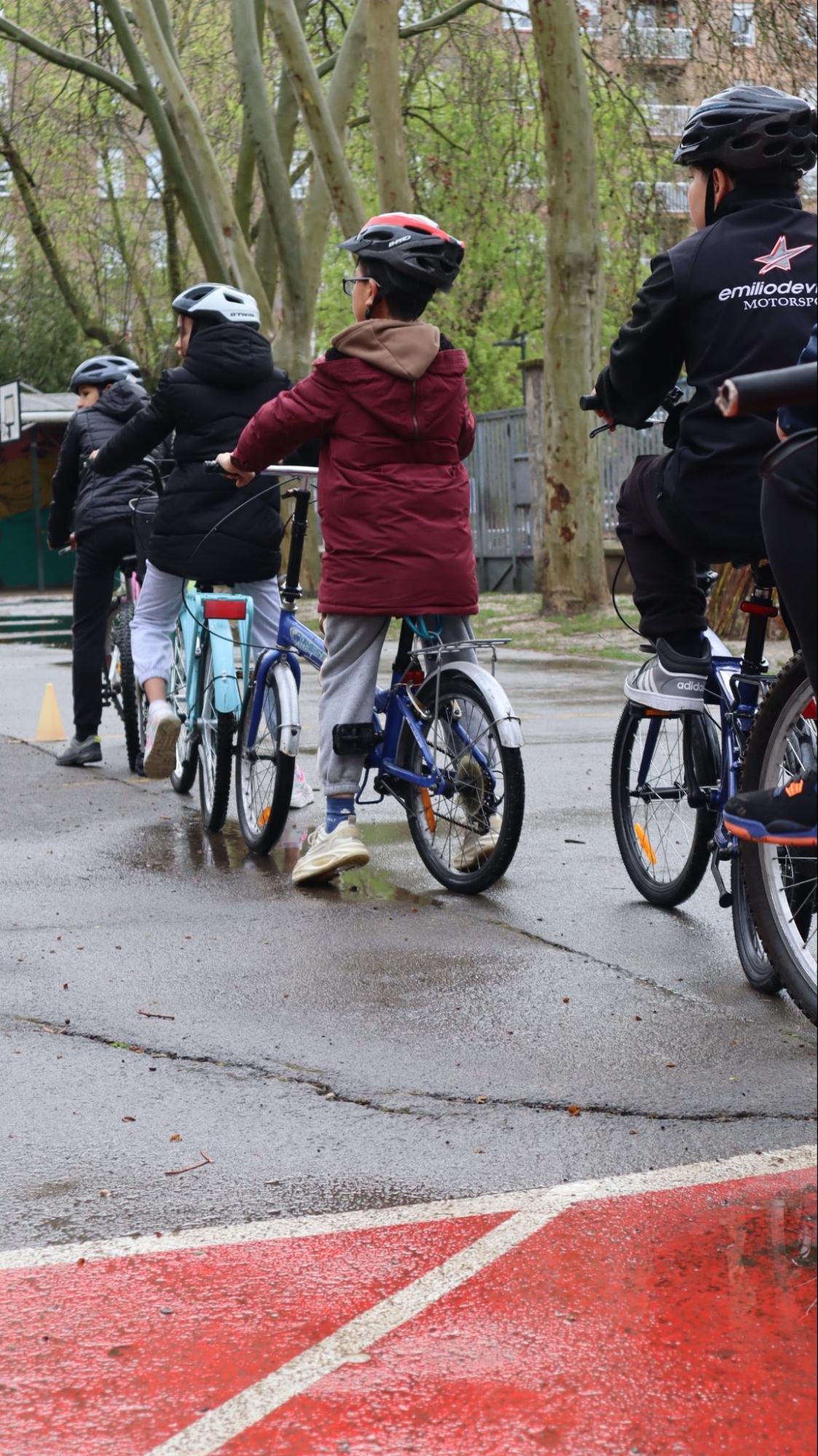 Alumnado en bici en el patio del colegio, de espaldas, con casco